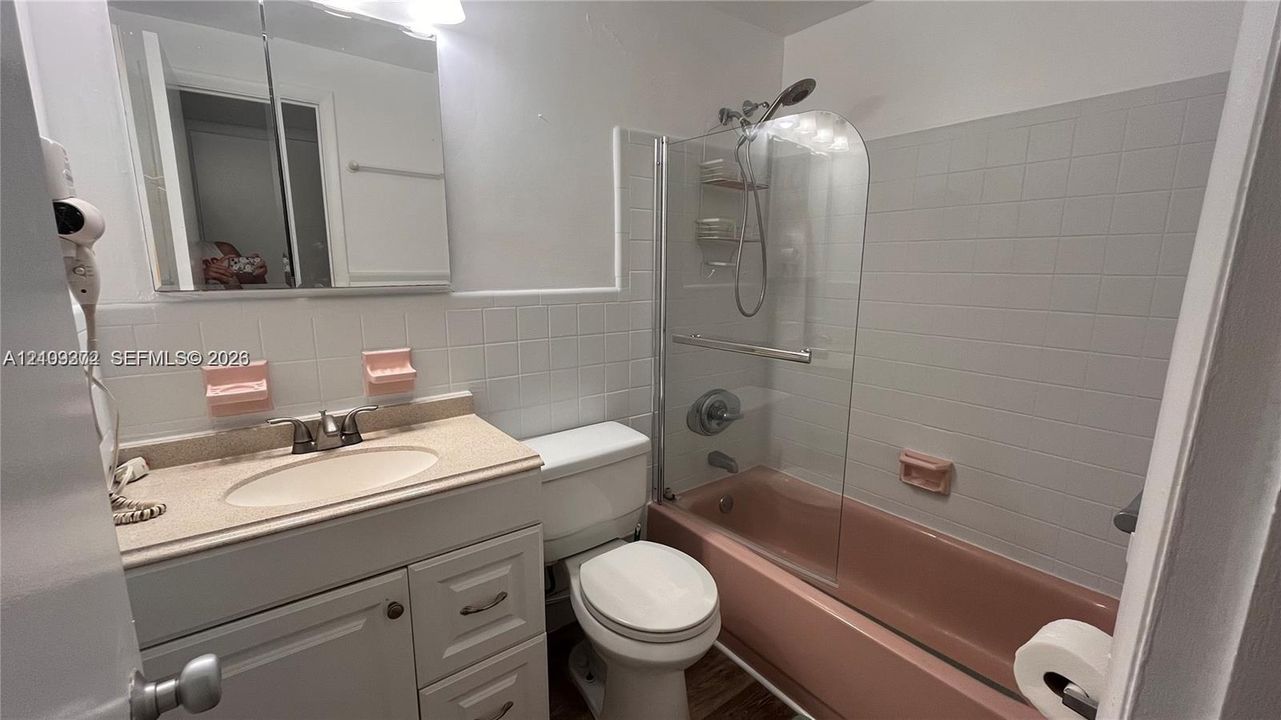 Bathroom featuring a vanity cabinet, integrated sink, mirrored medicine cabinet, and a bathtub with a glass panel enclosure and wall-mounted shower fixture