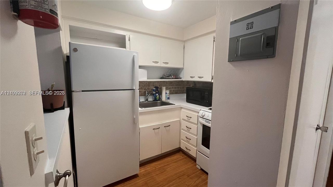 Kitchen featuring white cabinetry, wood-finish flooring, metal sink with faucet, and white appliances