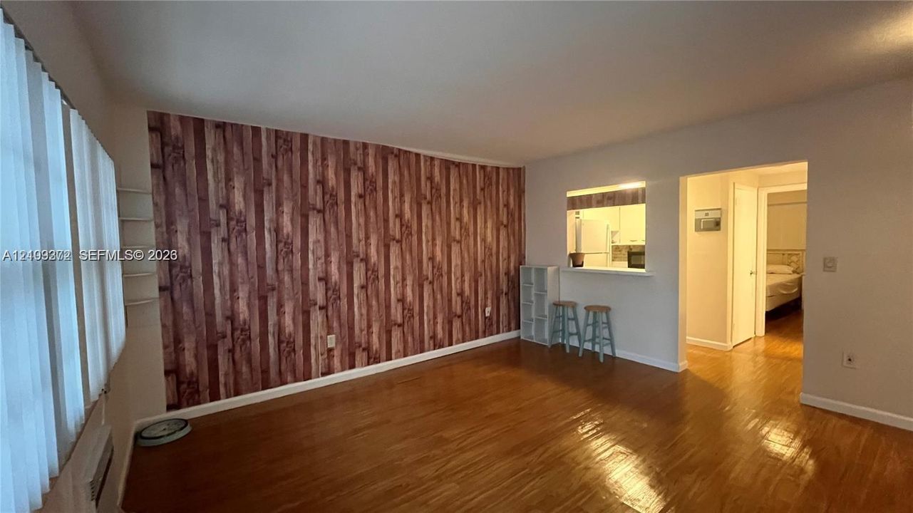 Interior space featuring wood-finish flooring, a wood-paneled accent wall, and a passthrough opening to the kitchen