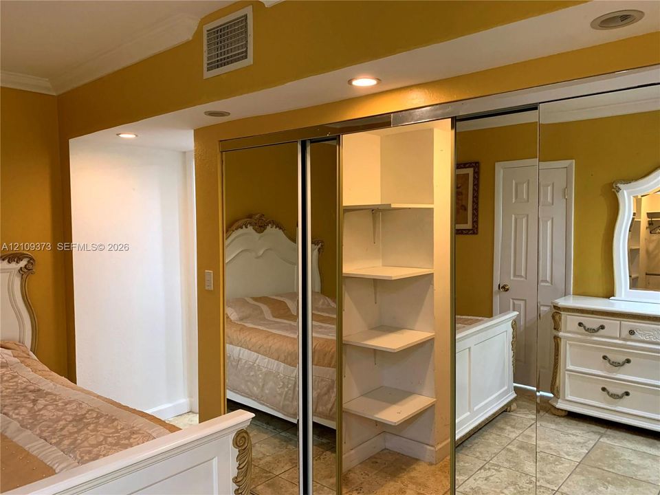 Sliding mirror-panel closet doors featuring built-in shelving, tile flooring, recessed ceiling lighting, and crown molding