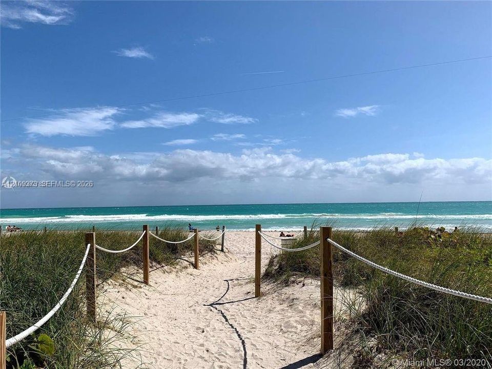 Sandy beach access featuring a sand pathway, wood post-and-rope perimeter, and coastal dune vegetation