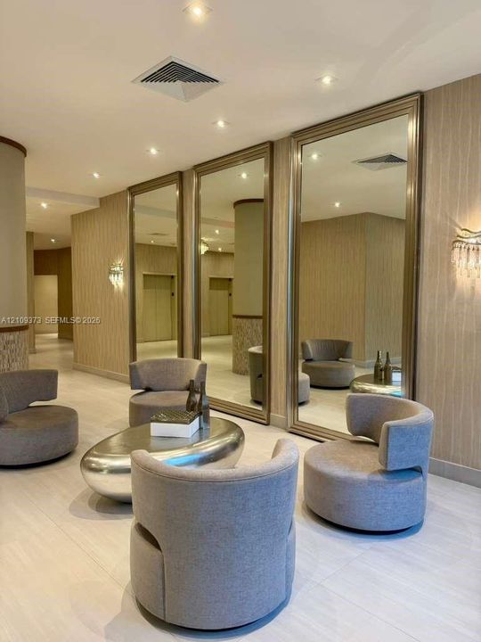 Large, floor-to-ceiling wall mirrors with metallic frames, textured vertical-pattern wall coverings, recessed ceiling lighting, and wall-mounted sconces