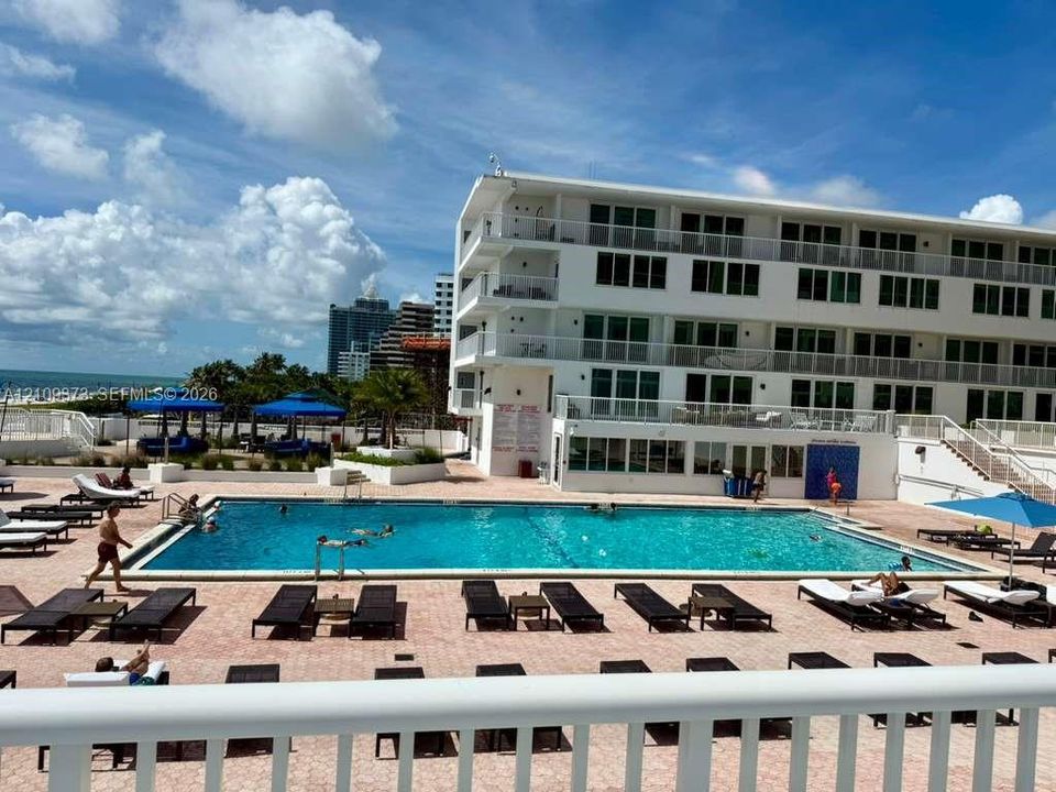Multi-story residential building featuring a rectangular swimming pool, expansive paved pool deck, and private balcony railings