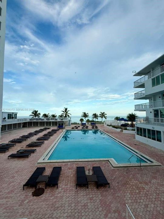 Rectangular swimming pool featuring a concrete deck, multi-level balconies, and water horizon backdrop