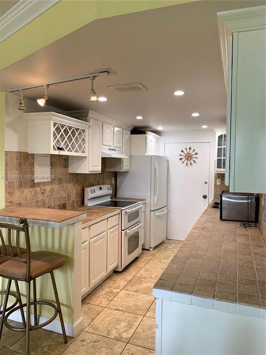 Kitchen featuring white cabinetry with lattice detail, tiled countertops, tile backsplash, tile flooring, and track lighting