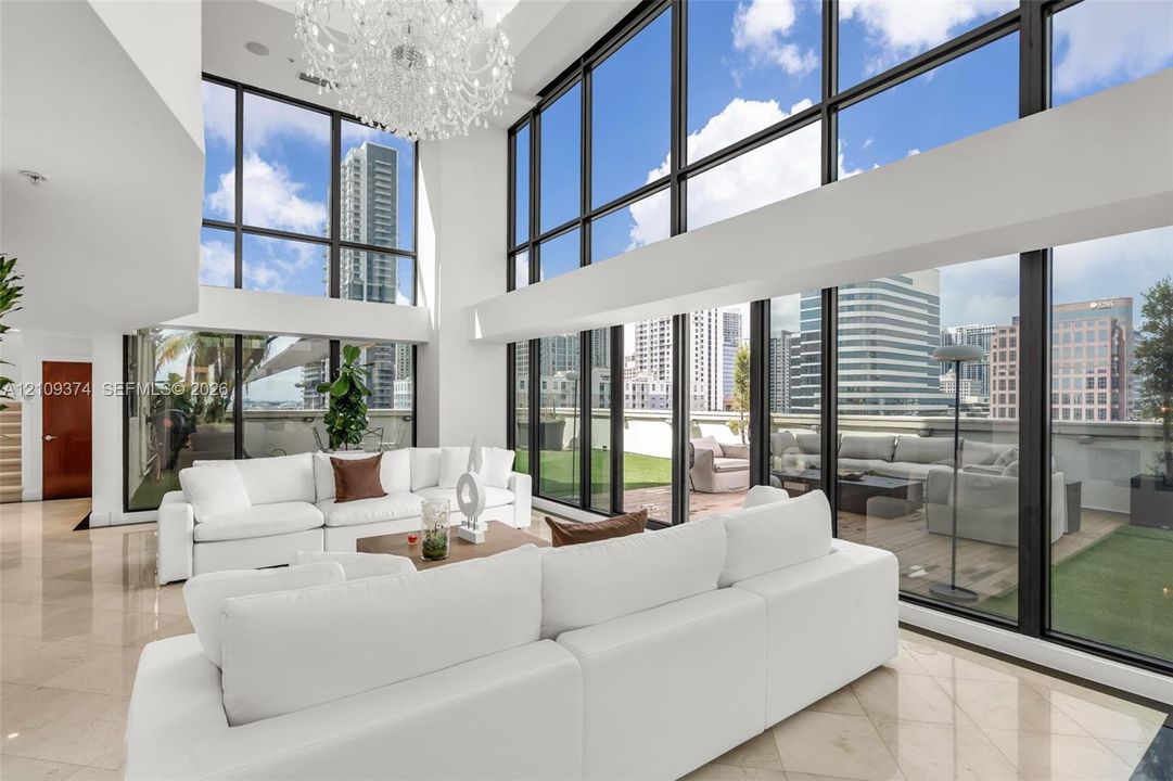 Double-height ceiling, floor-to-ceiling windows, polished stone flooring, custom crystal chandelier, and integrated exterior terrace