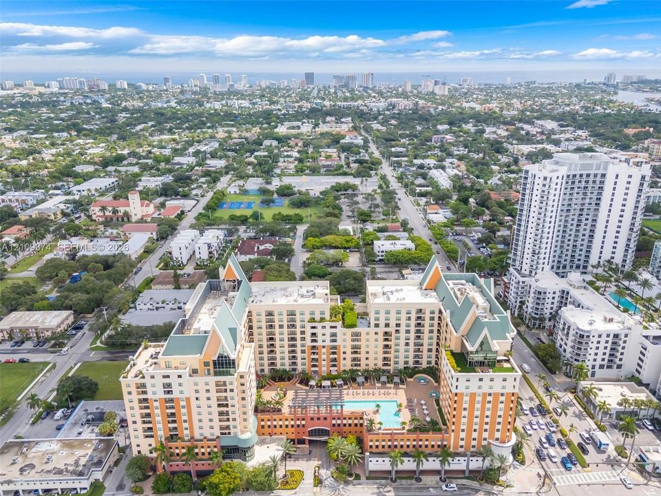 Aerial perspective of a multi-story residential complex featuring a central outdoor swimming pool, terracotta-toned facade, decorative pitched roofing, and expansive terrace levels