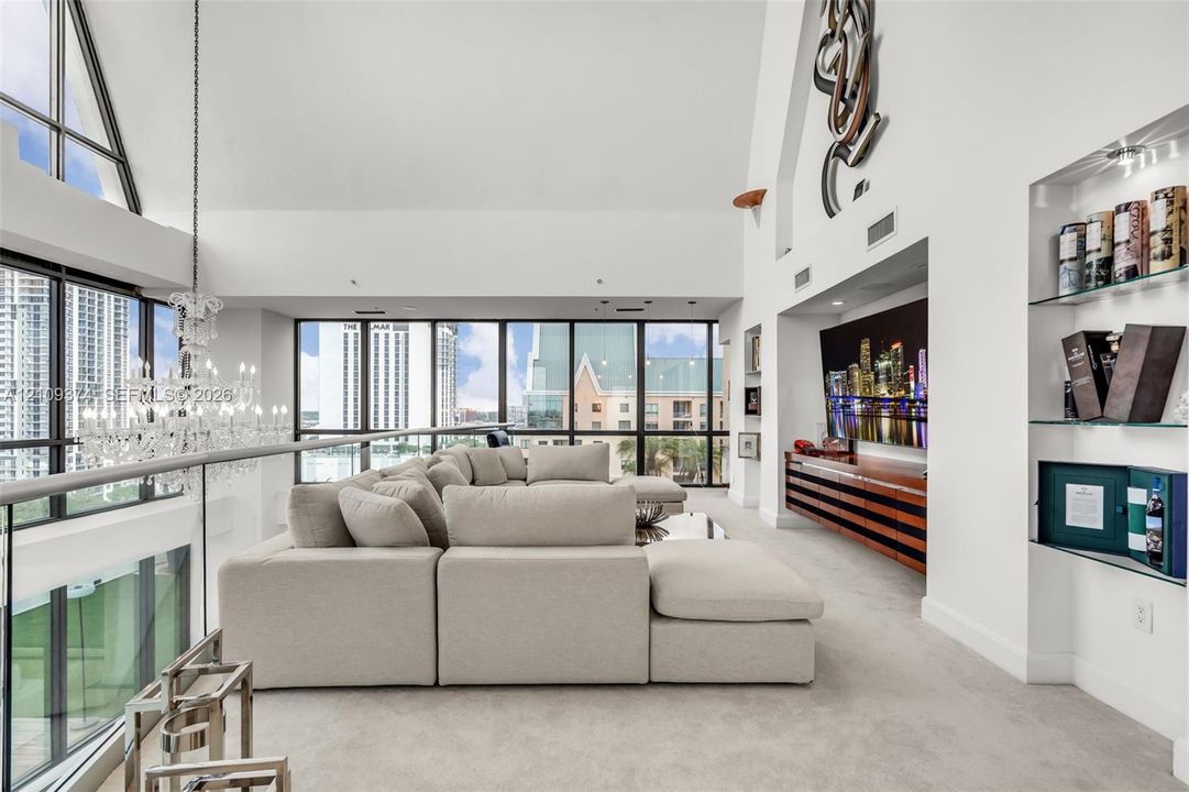 Vaulted ceilings with floor-to-ceiling windows, crystal chandelier, built-in horizontal wood-slat cabinetry, and integrated glass shelving
