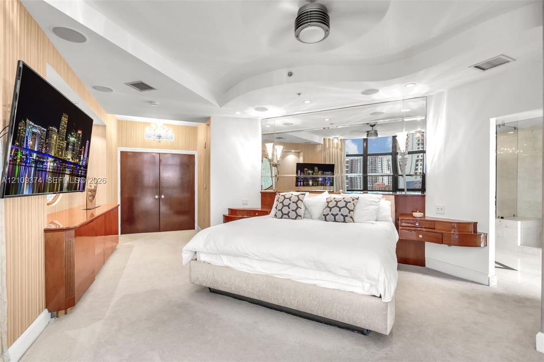 Tray ceiling with integrated lighting, mirrored wall accents, built-in mahogany-finish cabinetry, neutral carpeting, and multi-paned windows