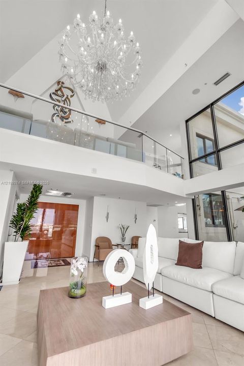 Two-story foyer featuring vaulted ceilings, floor-to-ceiling windows, a large multi-tiered crystal chandelier, and a glass-paneled mezzanine railing