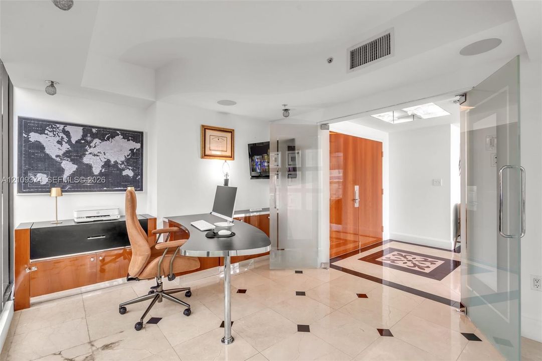 Light-filled room featuring large-format stone flooring with decorative inlay, custom wood-finish built-in cabinetry, frosted glass pivot entry doors, and recessed ceiling lighting