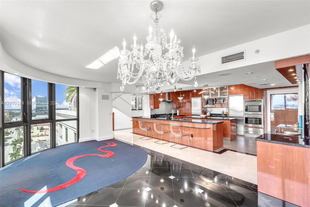 Kitchen featuring high-gloss wood cabinetry, dark stone countertops, built-in stainless steel appliances, a large center island, and an ornate crystal chandelier