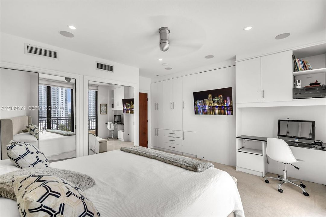 Built-in floor-to-ceiling cabinetry, recessed lighting, integrated desk workspace, mirrored closet doors, and flush-mount ceiling fan