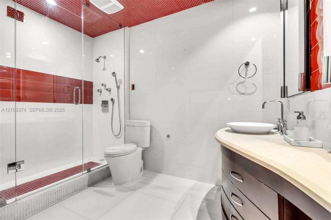 Bathroom featuring a glass-enclosed shower with multi-head fixtures and decorative tile accents, a curved wood-finish vanity with a vessel sink, and a high-profile toilet