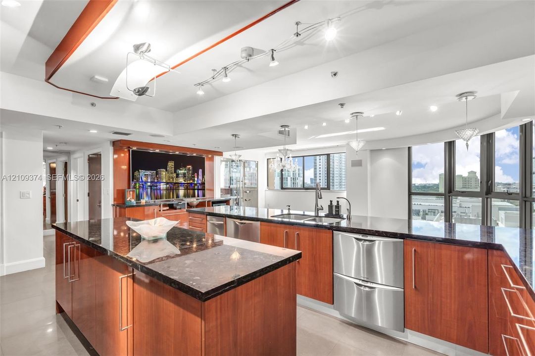 Kitchen featuring wood-veneer cabinetry, stone countertops, stainless steel appliances, tiered tray ceiling with recessed lighting, and floor-to-ceiling windows