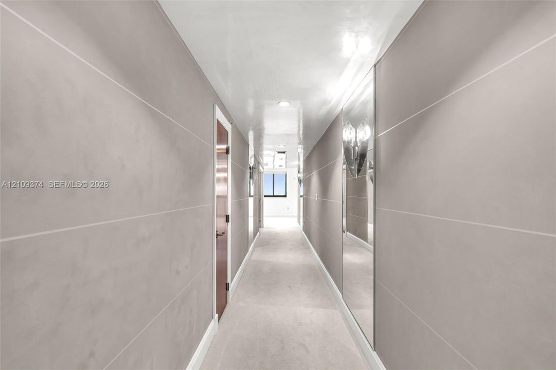 Hallway featuring matte grey paneling with horizontal reveals, inset floor-to-ceiling mirrored walls, and recessed ceiling lighting