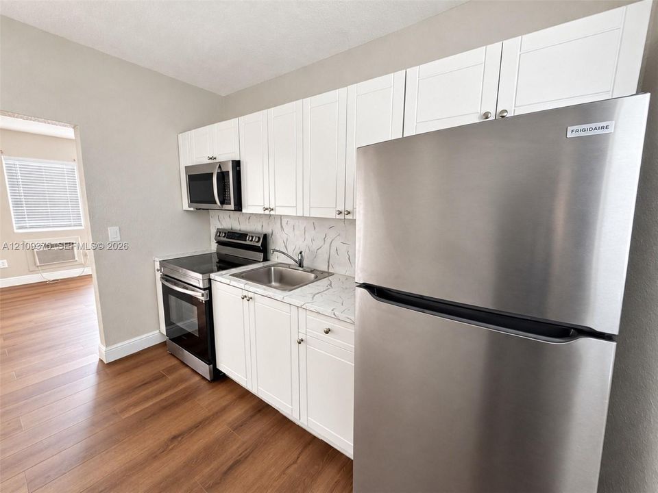 Kitchen featuring white shaker-style cabinetry, stone-patterned countertops, a stainless steel refrigerator, a built-in microwave, and wood-finish flooring
