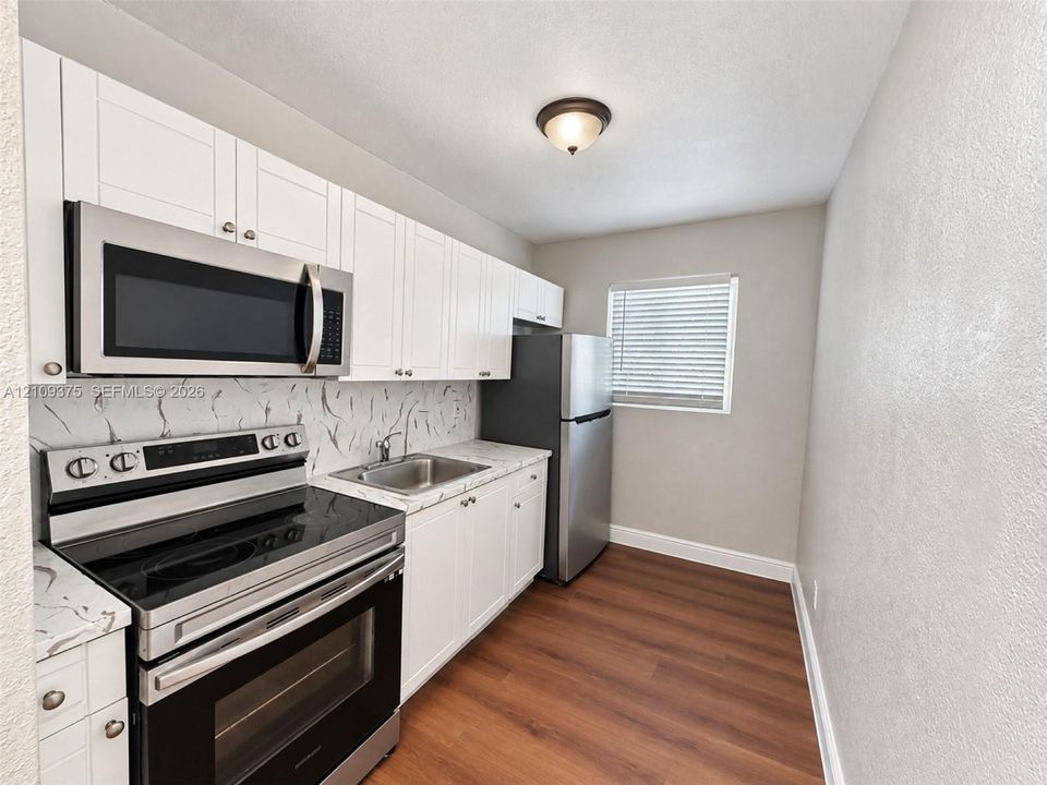 Kitchen featuring white shaker-style cabinetry, stainless steel appliances, patterned stone-finish countertops, tile backsplash, and wood-finish flooring