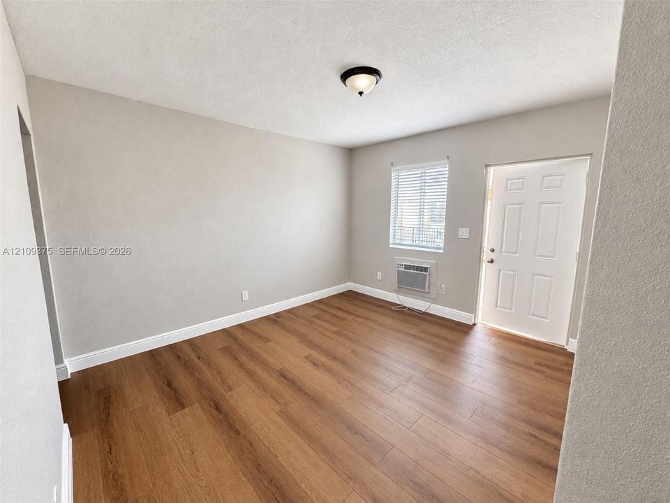 Room featuring wood-finish flooring, neutral wall paint, a six-panel entry door, and a flush-mount ceiling light fixture