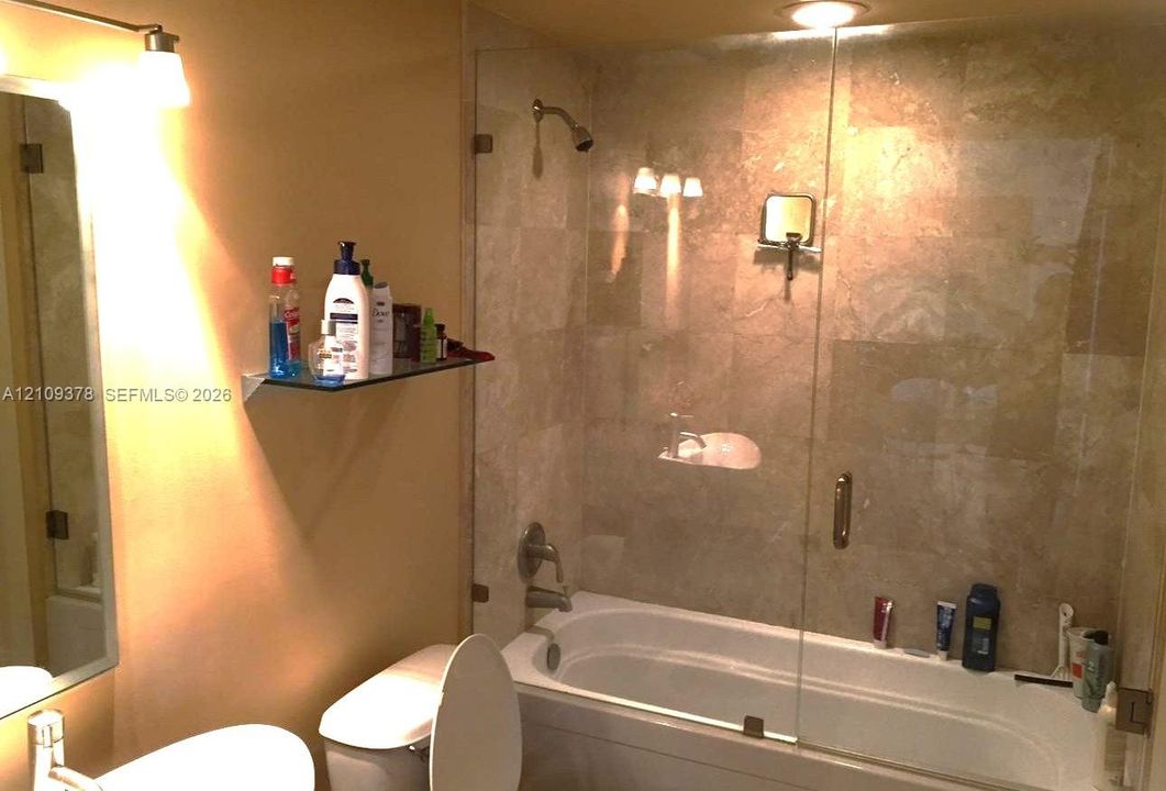 Full-height tile shower surround with a frameless glass panel, built-in glass shelving, vanity mirror with wall-mounted lighting, and a recessed shower fixture