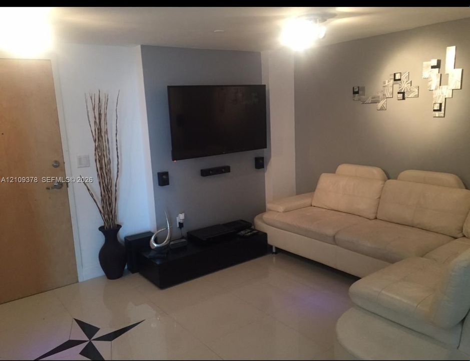 Interior space featuring large-format tile flooring, a recessed accent wall with integrated wall-mounted television, and flush-mount ceiling lighting