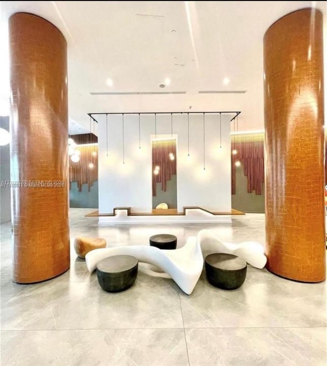 Large-scale textured metallic columns, polished tile flooring, recessed ceiling lighting, custom wall-integrated wood seating, and vertical pendant lighting fixtures