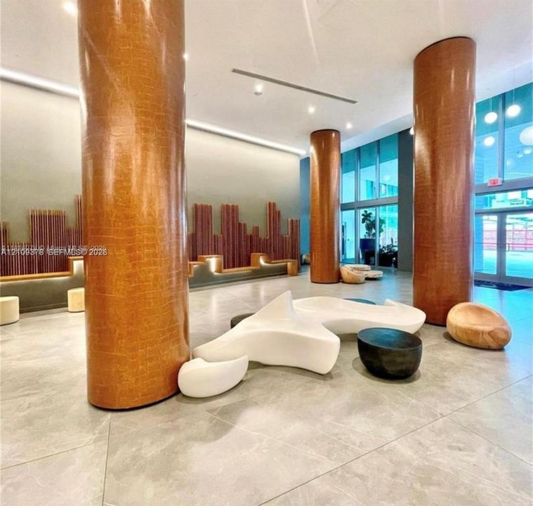 Lobby featuring floor-to-ceiling textured structural columns, large-format tile flooring, recessed cove lighting, and a linear wall installation with integrated accent lighting