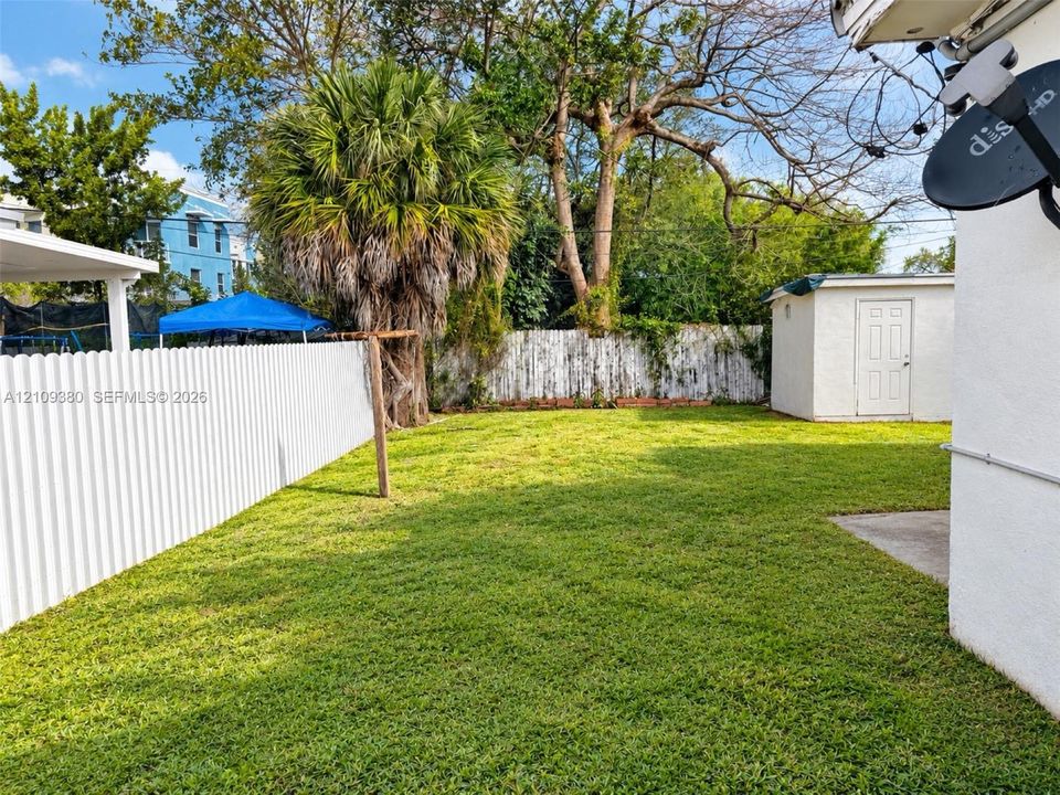 Fenced backyard featuring a manicured lawn, detached storage structure, and mature vegetation