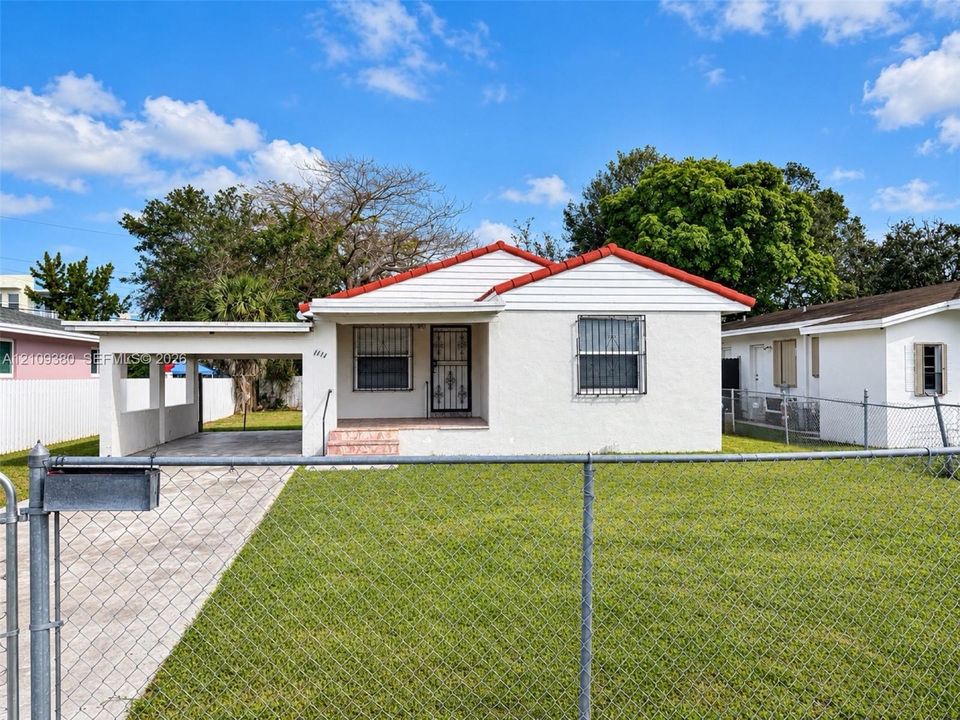 Stucco exterior featuring a red tile roof, attached covered carport, concrete driveway, and chain-link perimeter fencing