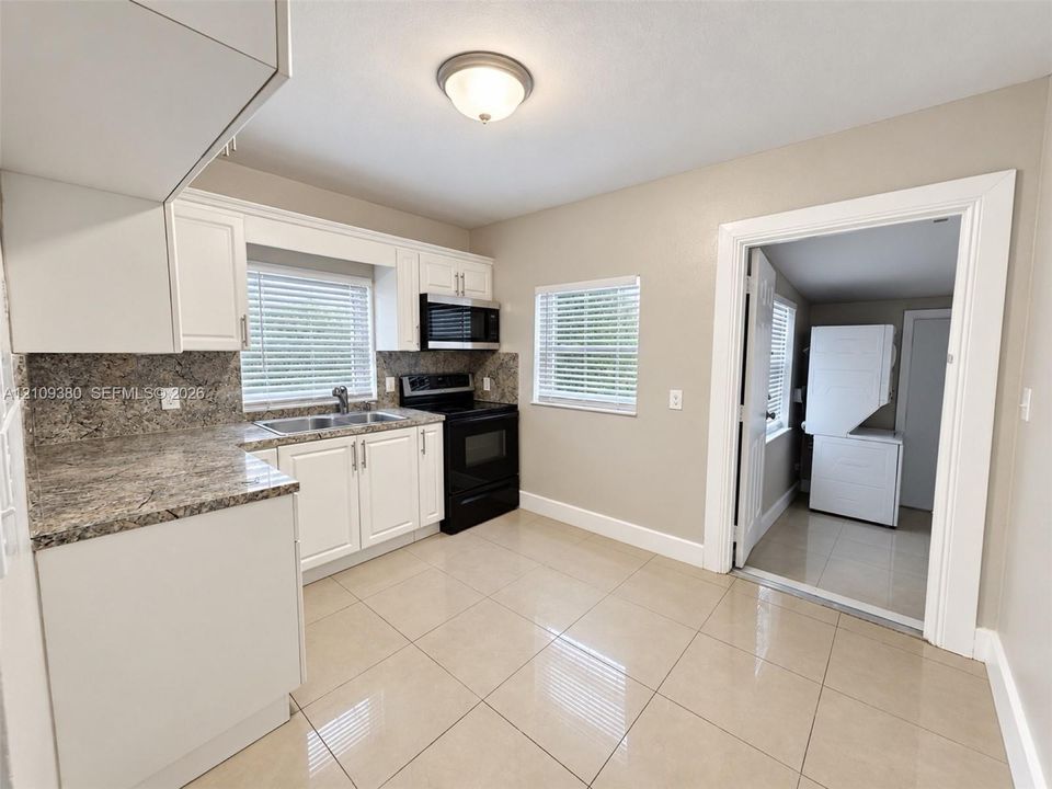 Kitchen featuring white shaker-style cabinetry, stone-surface countertops, tile flooring, and integrated black appliances