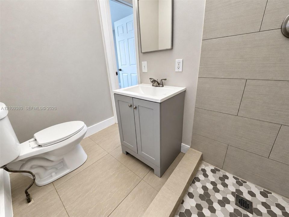 Grey vanity featuring a white countertop and basin, walk-in shower with large-format wall tile and hexagonal floor tile, and ceramic floor tile