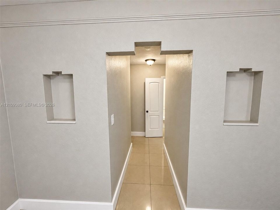 Neutral wall finishes featuring symmetrical recessed wall niches, crown molding, and large-format tile flooring