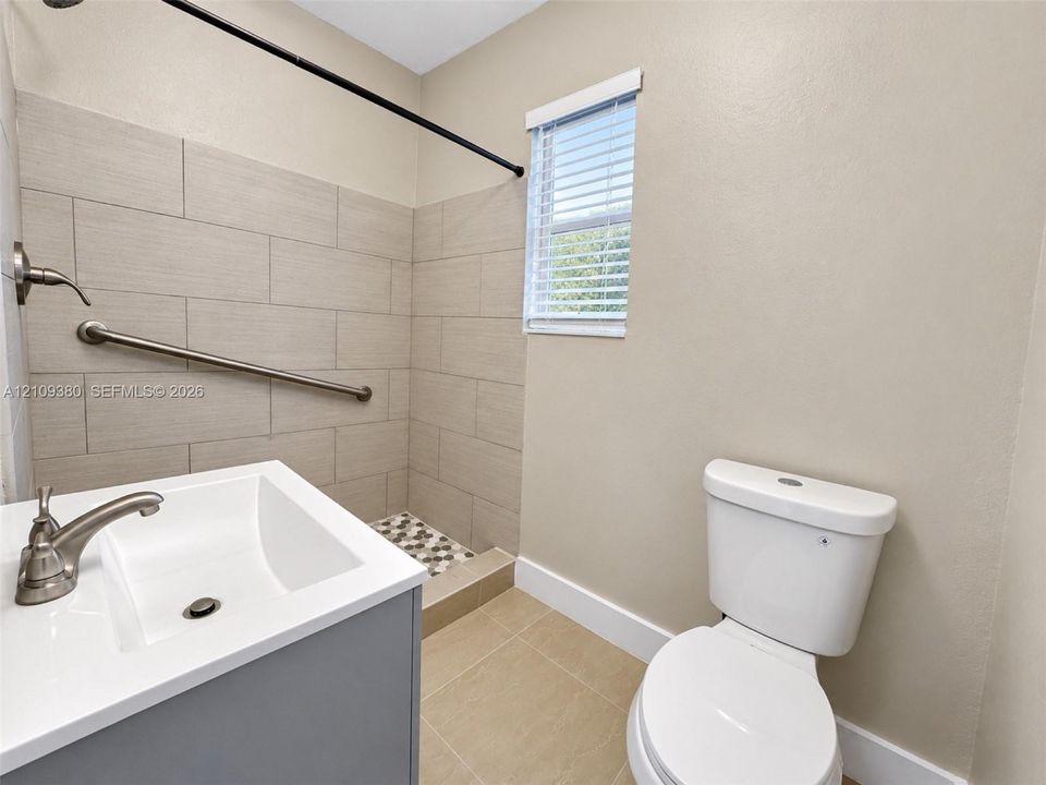 Bathroom featuring a gray vanity with a white countertop, beige large-format wall tile, shower stall with a grab bar, and neutral floor tile