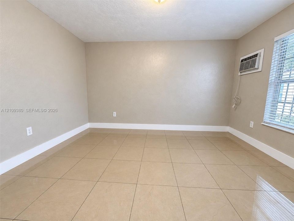 Room featuring neutral-toned tile flooring, light-colored walls, a ceiling-mounted light fixture, and a window with horizontal blinds