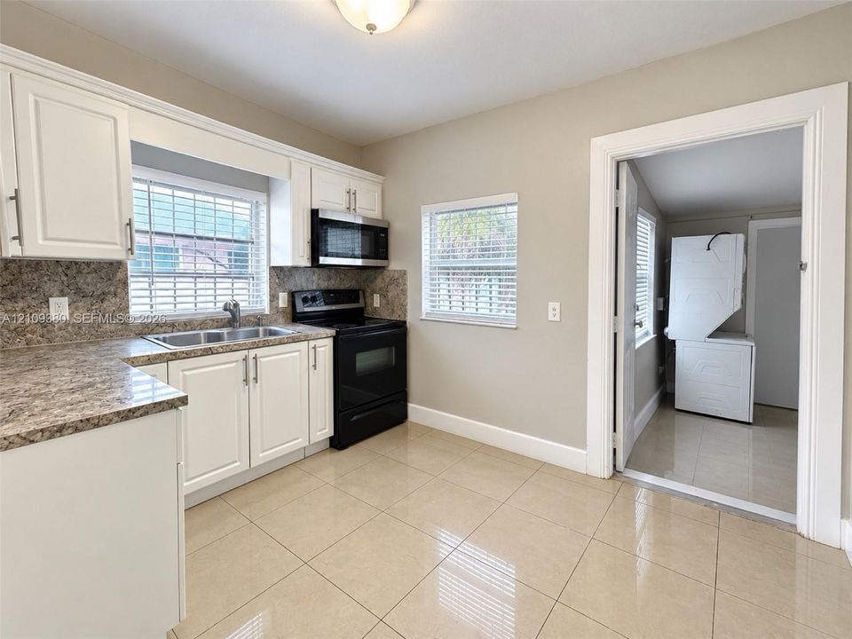 Kitchen featuring white cabinetry, stone-finish countertops, black appliances, tile flooring, and a dedicated laundry area