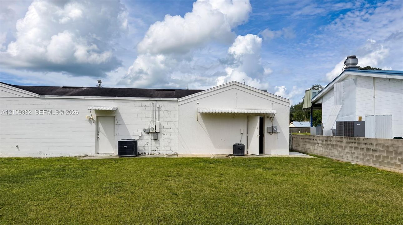 Exterior rear elevation featuring white painted masonry walls, metal awnings over entry points, and a concrete block perimeter wall
