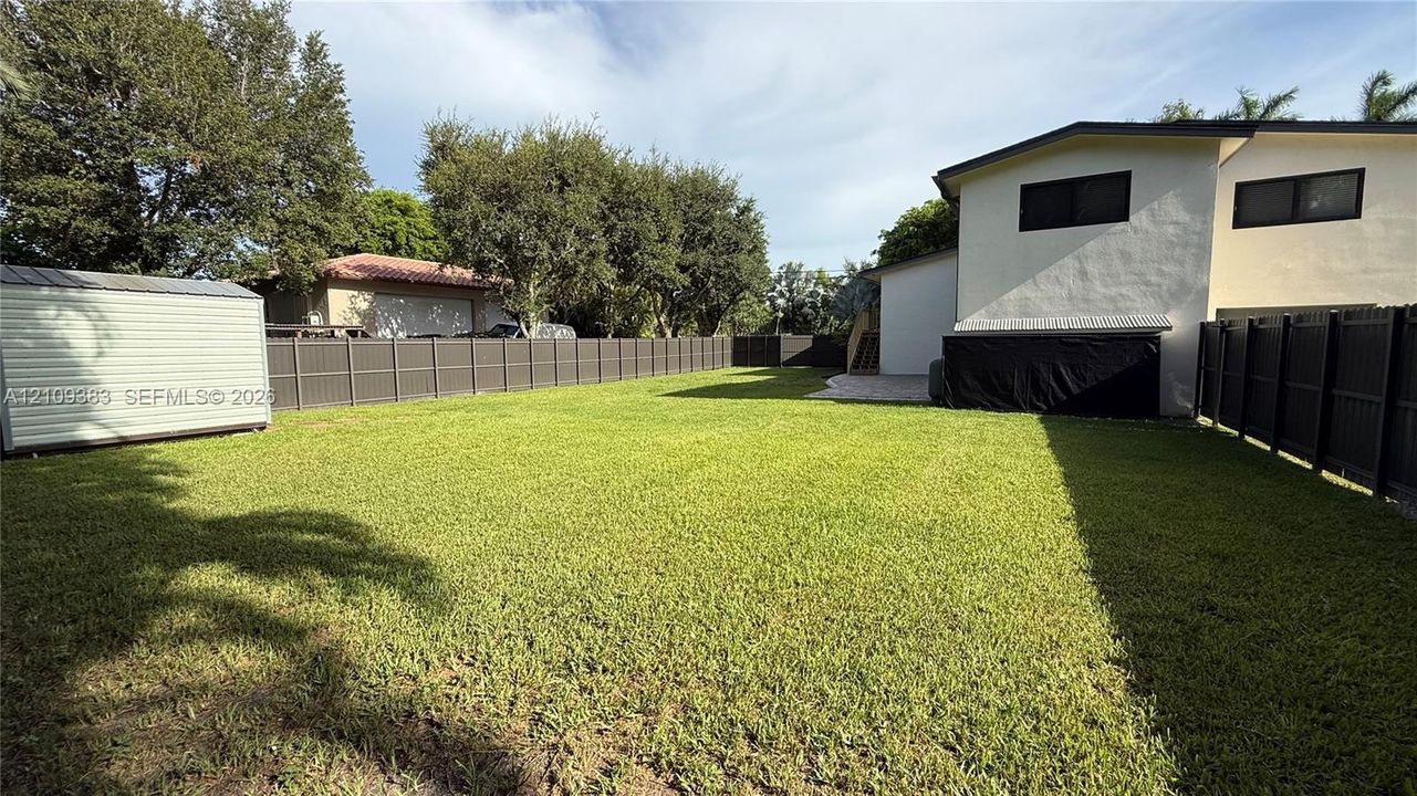 Spacious backyard featuring a manicured lawn, full-perimeter privacy fencing, and a detached storage structure