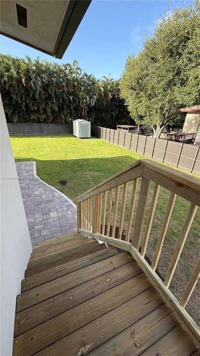 Backyard featuring a wood-plank deck, stone-paver walkway, fenced perimeter, and dedicated storage shed