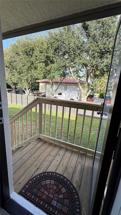 Wood-plank balcony with natural-finish wood railing and stairs, grass lawn, and perimeter fencing