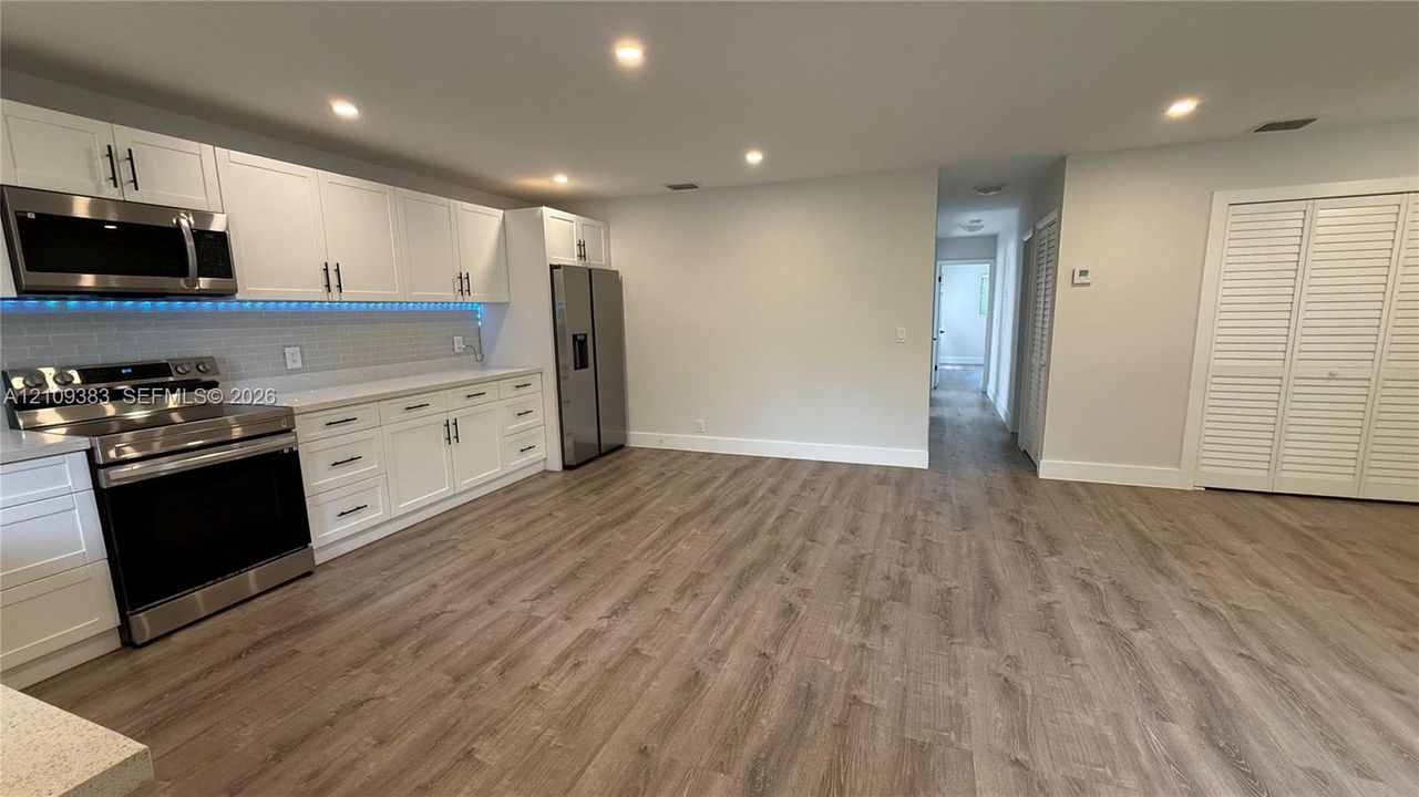 Kitchen featuring white shaker-style cabinetry, stainless steel appliances, recessed ceiling lighting, light-toned wood-finish flooring, and white louvered closet doors