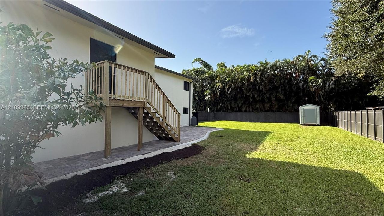 Expansive backyard featuring a manicured lawn, paved patio, wood-construction exterior staircase, and perimeter fencing