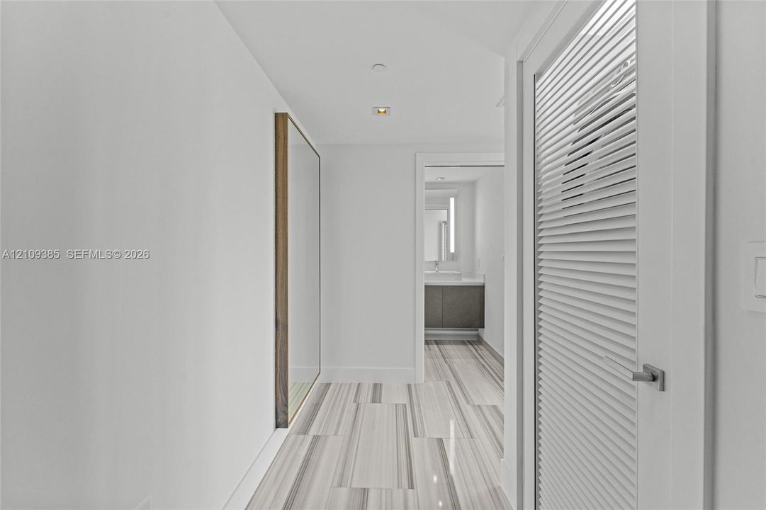 Neutral-toned stone flooring throughout, featuring a wall-mounted vanity with a rectangular vessel sink and an integrated mirror with side lighting