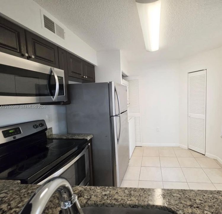 Kitchen featuring dark-finish cabinetry, stone countertops, stainless steel appliances, and tile flooring