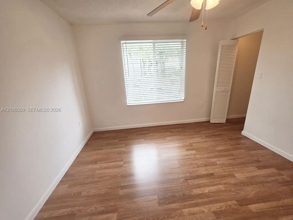 Room featuring wood-finish flooring and a multi-blade ceiling fan with integrated lighting