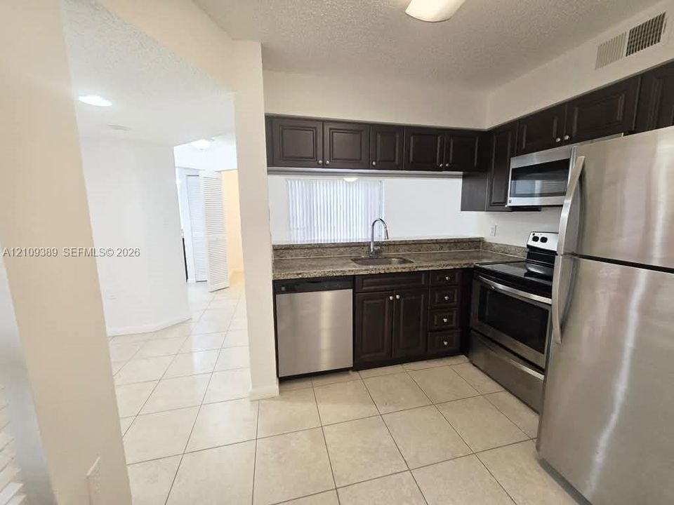 Kitchen featuring dark-finish cabinetry, stone-style countertops, stainless steel appliances, and a single-basin undermount sink with a gooseneck faucet