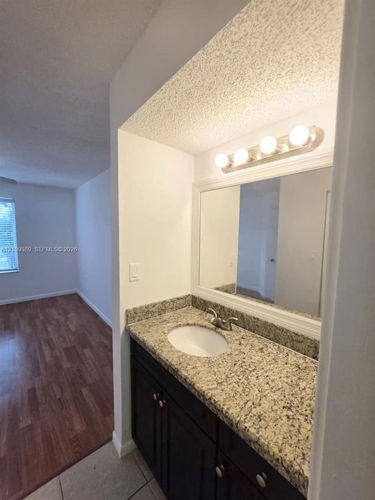 Vanity featuring a stone-surface countertop with an integrated oval sink, dark wood-finish cabinetry, framed vanity mirror, and multi-bulb wall-mounted lighting