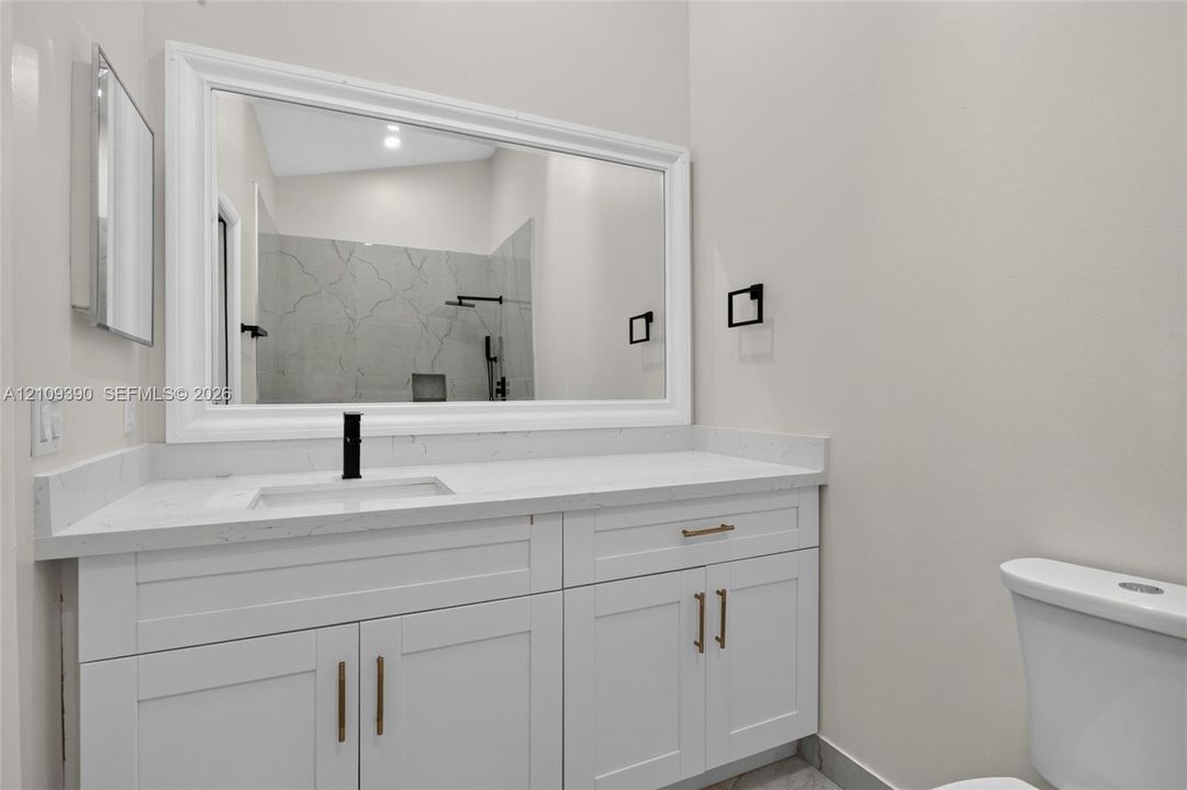 White cabinetry with brass-toned hardware, quartz countertop, undermount sink with matte black faucet, and framed vanity mirror