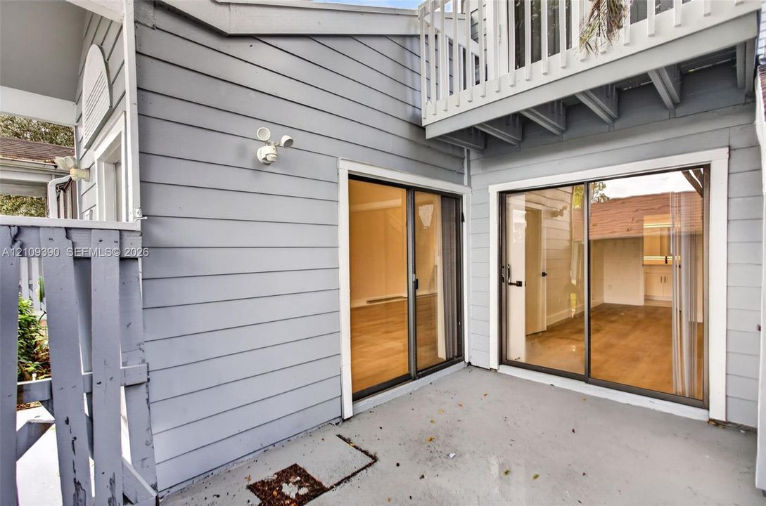 Exterior patio space featuring horizontal lap siding, two sets of glass sliding doors, and a wood-slat upper balcony