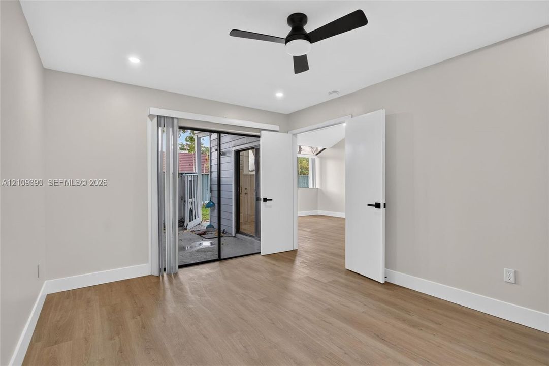 Room featuring wood-finish flooring, recessed lighting, a modern ceiling fan with integrated light, sliding glass doors, and dual-panel doors with matte black hardware