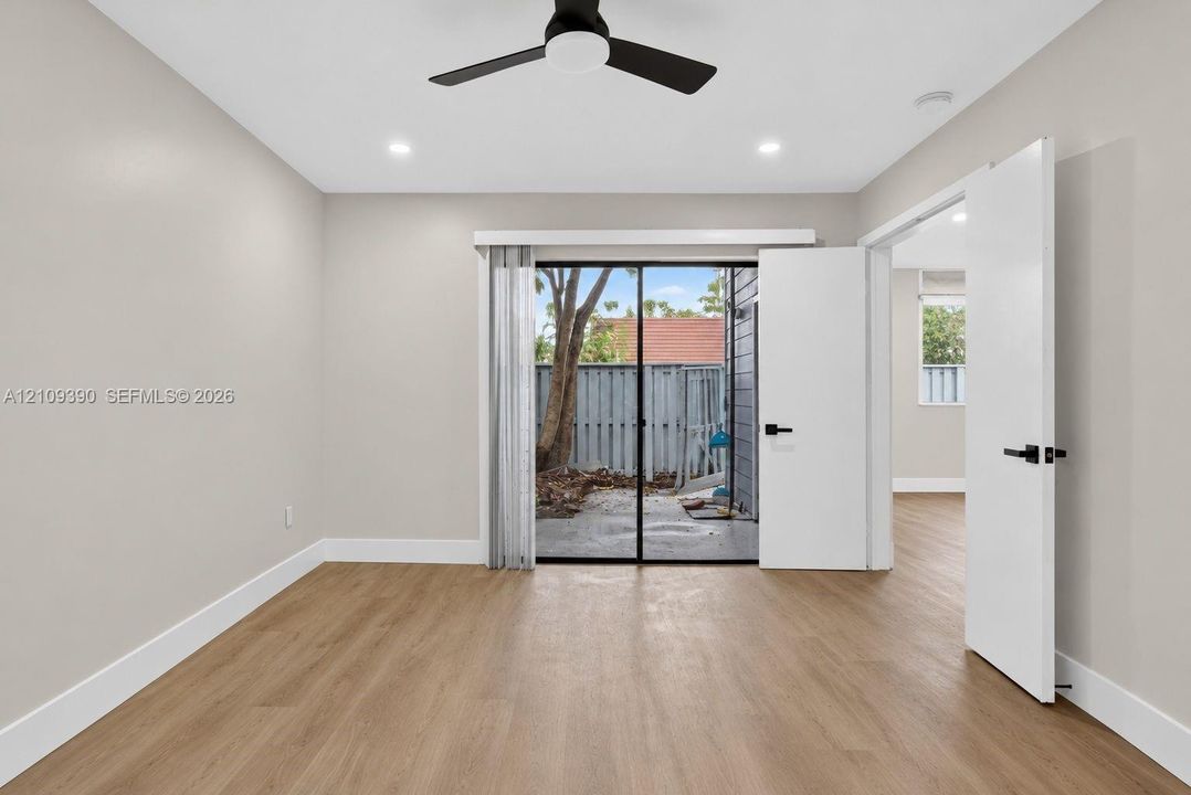 Neutral-toned room featuring wood-finish flooring, a matte black ceiling fan, recessed lighting, and a sliding glass door providing external access